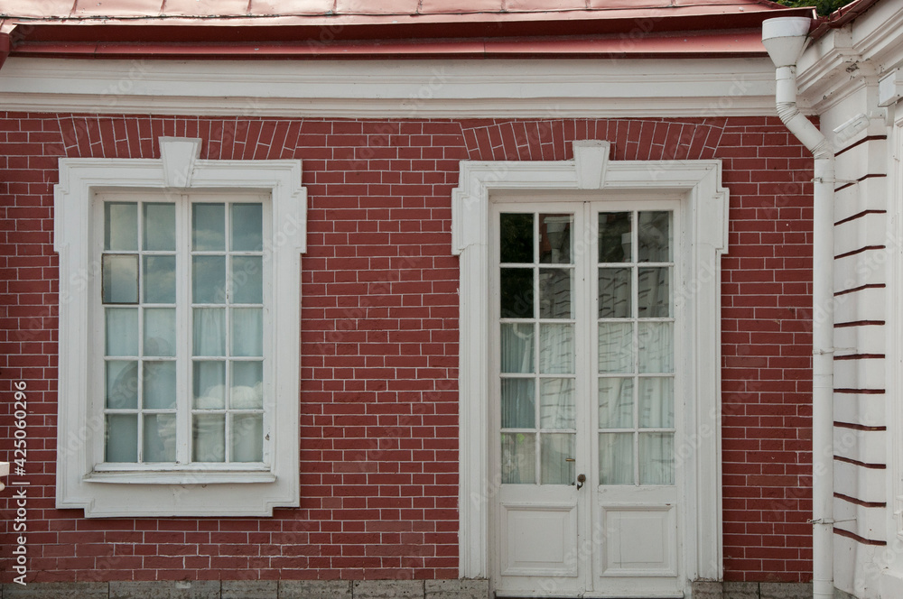 White framed windows and doors in the wall of the red brick house. Vintage glass windows of the old building. Classicism in architecture. White framed windows and doors in the wall of the red brick house. Vintage glass windows of the old building. Classicism in architecture.