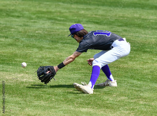 Action photo of athletic high school baseball player making an amazing play during a baseball game