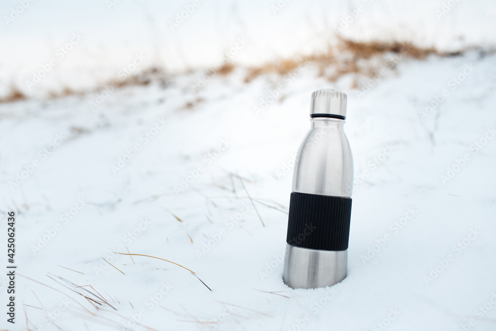 Close-up of steel reusable thermo water bottle in snow. - obrazy, fototapety, plakaty 