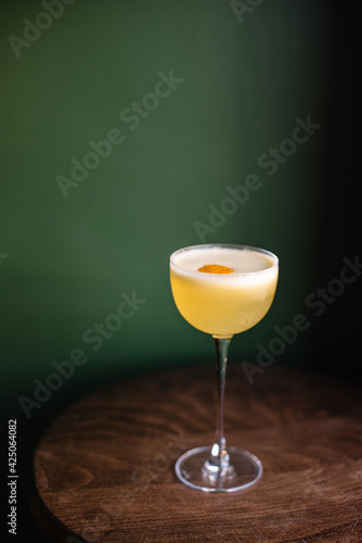 Whiskey sour cocktail decorated with lemon zest. Green color background.	