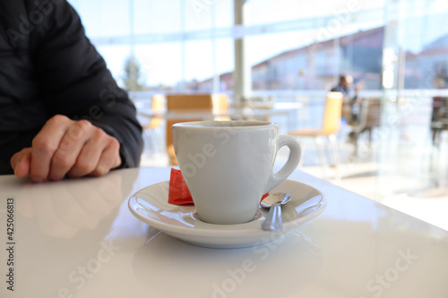 A cup of coffee on a table in a cafe against the background of a male hand and a silhouette of a guest.
