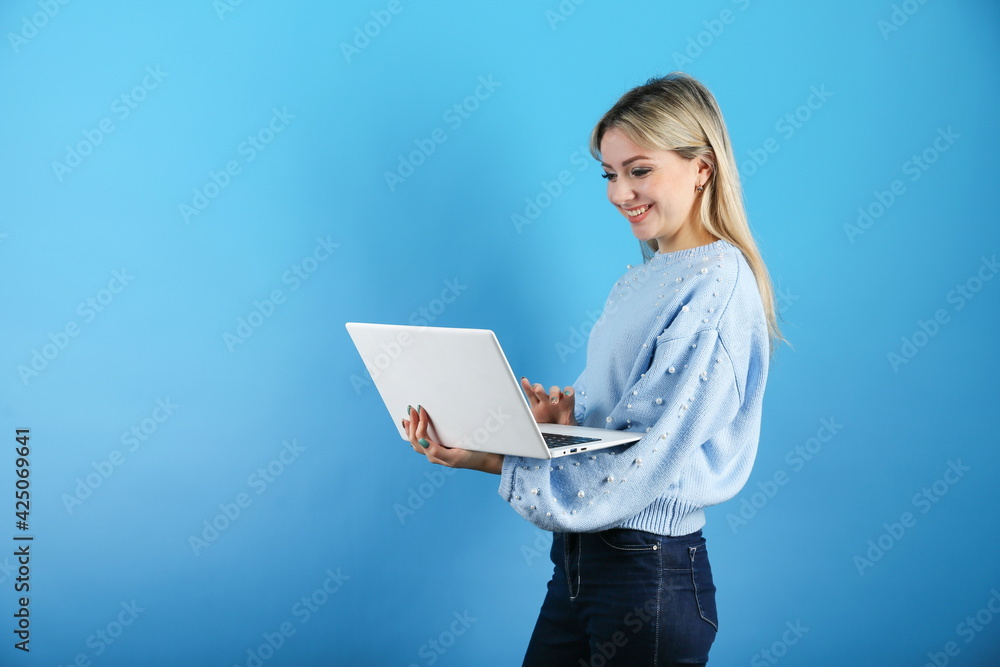 smiling woman using laptop on color background with copy space. young woman holding a laptop on a blue background. video communication concept smiling woman using laptop on color background with copy space. young woman holding a laptop on a blue background. video communication concept