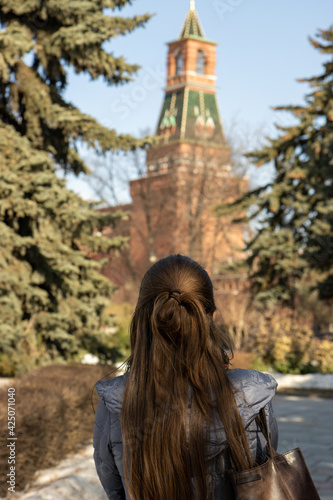 Young woman is watching Kremlin tower, view from back. Trees and blue sky on the background 
