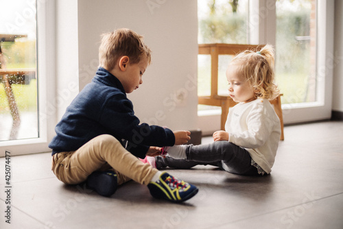 Bild auf Leinwand Grand frère aide sa petite sœur à mettre ses chaussures