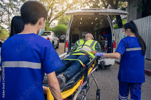 Paramedic team transfer man on ambulance stretcher into emergency car.