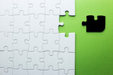 white puzzle with one piece missing to complete, but the missing piece is black and not the right shape. green background with copy space
