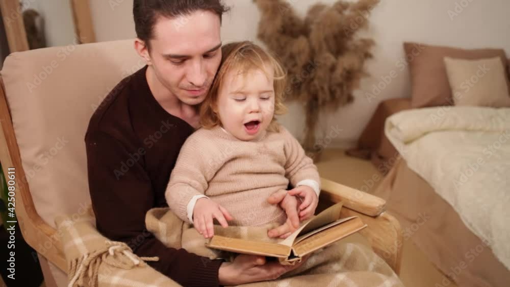 young father and daughter read a book, have fun, laugh. Home family evening, comfort and love. A man and a girl sit in a rocking chair, beige interior. Yawns young father and daughter read a book, have fun, laugh. Home family evening, comfort and love. A man and a girl sit in a rocking chair, beige interior. Yawns