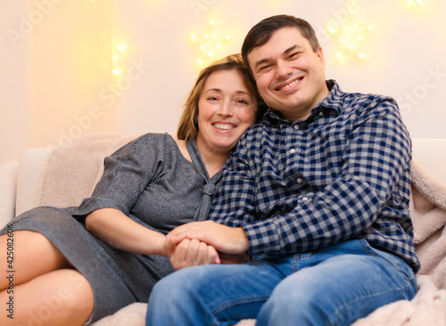 portrait of adult romantic couple sitting on a couch at home, holiday lights on a wall