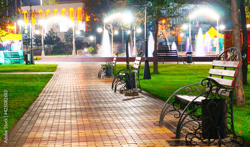 autumn city park at night, trees with yellow leaves, street lights and benches © soleg