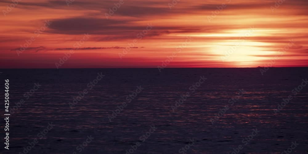 Time-lapse of perfect orange-red sunset. Bright sun beyond the clouds approach with dark sea waves. Cargo ship move on the background Time-lapse of perfect orange-red sunset. Bright sun beyond the clouds approach with dark sea waves. Cargo ship move on the background
