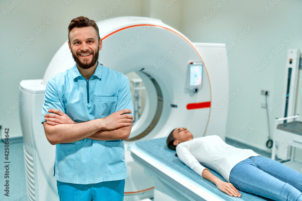A smiling radiologist stands next to a patient lying on a CT or MRI machine. In a medical laboratory with high-tech equipment. A smiling radiologist stands next to a patient lying on a CT or MRI machine. In a medical laboratory with high-tech equipment.