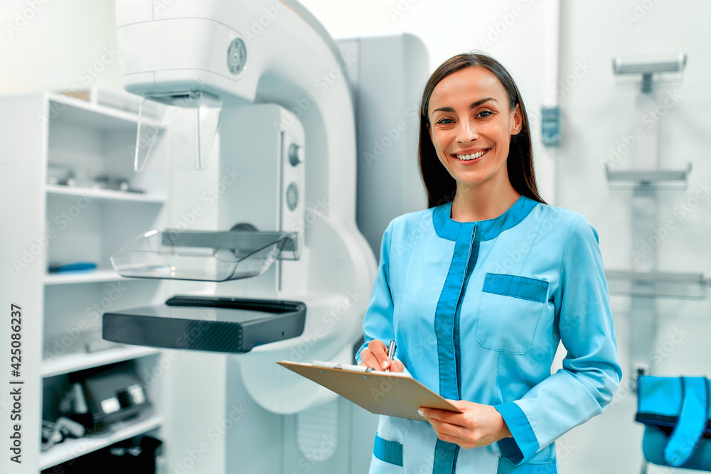 A female doctor with a patient card standing near the mammography apparatus. Health care and medical women concept. A female doctor with a patient card standing near the mammography apparatus. Health care and medical women concept.