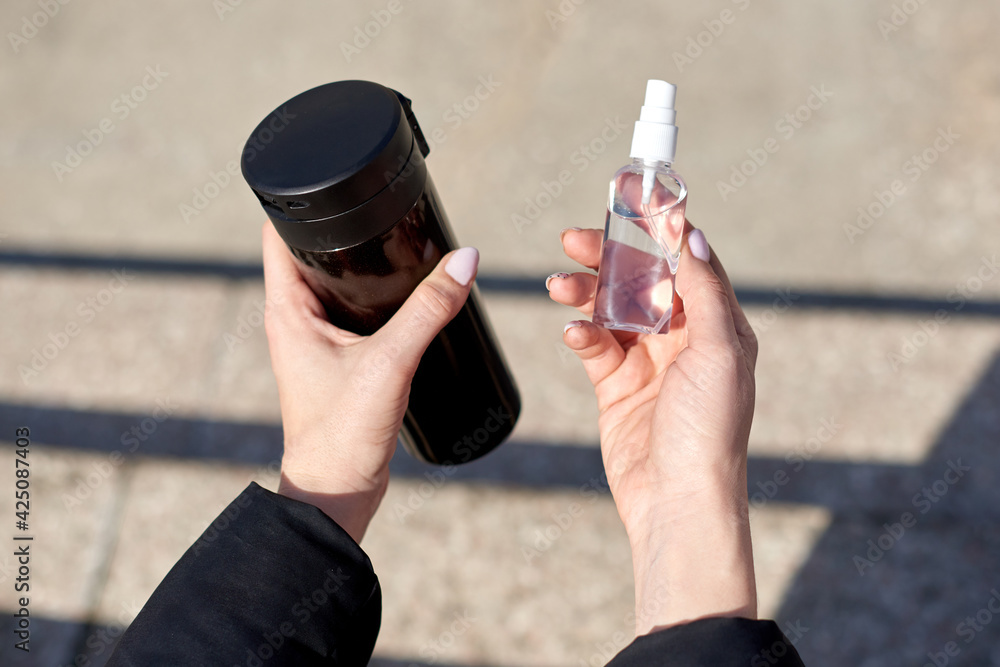 Naklejka premium hands hold alcohol antiseptic and mug of tea, prevent against infection of Covid-19 outbreak,woman washing hands with hand sanitizer to avoid contaminating with Corona virus