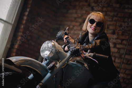 Happy woman motorbiker in a sunglasses is sitting on the old motorcycle.