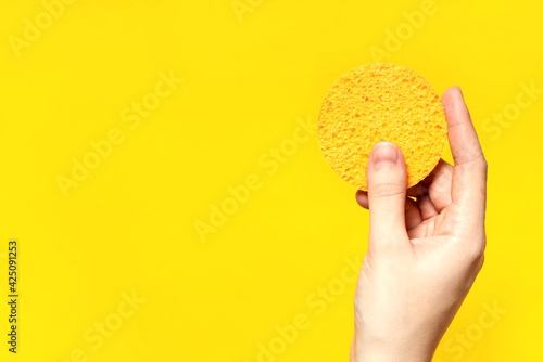 Round cosmetic sponge pad for face make up cleaning in hand on yellow background.