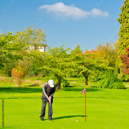 Male golf player pitching off golf ball to the hole, wonderful sky and cloud formation in background.