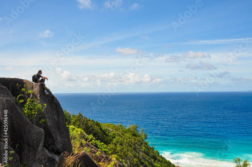 One tourist man sitting on a rock on the top of the hill in the viewpoint with the Indian ocean in the background