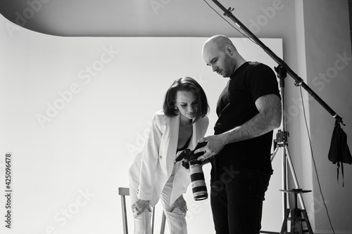 Fashion photography in a photo studio. Professional male photographer taking pictures of beautiful woman model on camera, black and white backstage photo