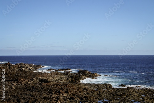 Playa de rocas volcánicas en el sur de la isla de Tenerife, Islas Canarias, España. Olas golpeando las rocas en un día de mar en calma.