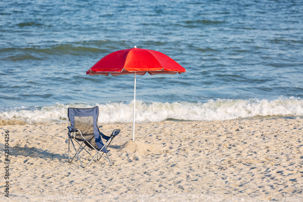 Red beach umbrella and camp chair on sand with waves in the background