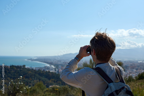 A young caucasian male looking at a sea view with binoculars