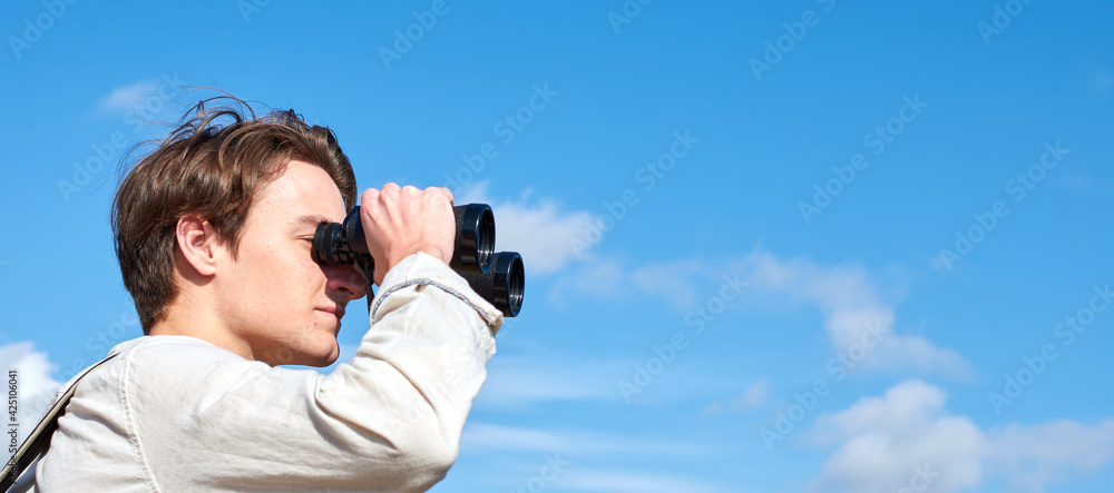 A side view of an attractive young explorer from Spain in a white shirt looking ahead through binoculars A side view of an attractive young explorer from Spain in a white shirt looking ahead through binoculars