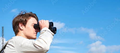 A side view of an attractive young explorer from Spain in a white shirt looking ahead through binoculars