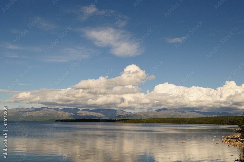 The peaks of the mountains, the Khibiny and a clear, bright sky with white clouds. View of the khibiny mountains from afar. Lake Imandra in summer. Kola Peninsula