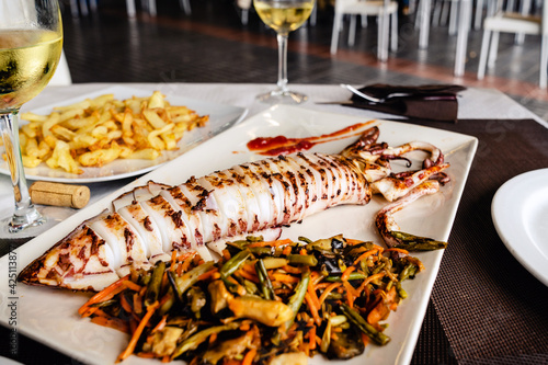 Grilled big squid (Calamar a la Plancha) and white wine - typical Spanish tapas. Gourmet dinner in the sea food restaurant in Getares, Algeciras. Southern Spain is a paradise for sea food lovers.