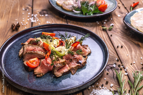 Beef tenderloin fried on fire with herbs, seasoned with spices, tomatoes. Wooden brown background decorated with rosemary, spices.