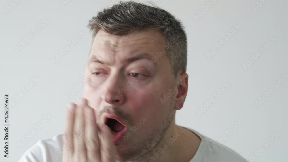 Morning hangover. Male hygiene. Grooming routine. Insomnia fatigue. Tired unkempt man checking eyes bad smelling breath touching face isolated on light neutral copy space background. Morning hangover. Male hygiene. Grooming routine. Insomnia fatigue. Tired unkempt man checking eyes bad smelling breath touching face isolated on light neutral copy space background.