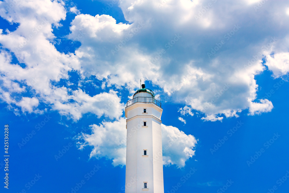 White lighthouse on a background of white clouds and blue sky.