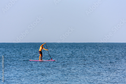 A man swims by sea on a sup-board, paddling with one oar.