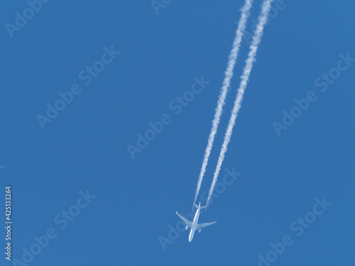  airplane flies in the blue sky and draws white vapor trails behind it © karegg