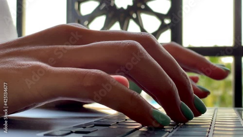 Remote job. Close up of female hands typing on keyboard while working on the laptop, sitting on the terrace. Freelance, telework, summertime concept. Slow motion