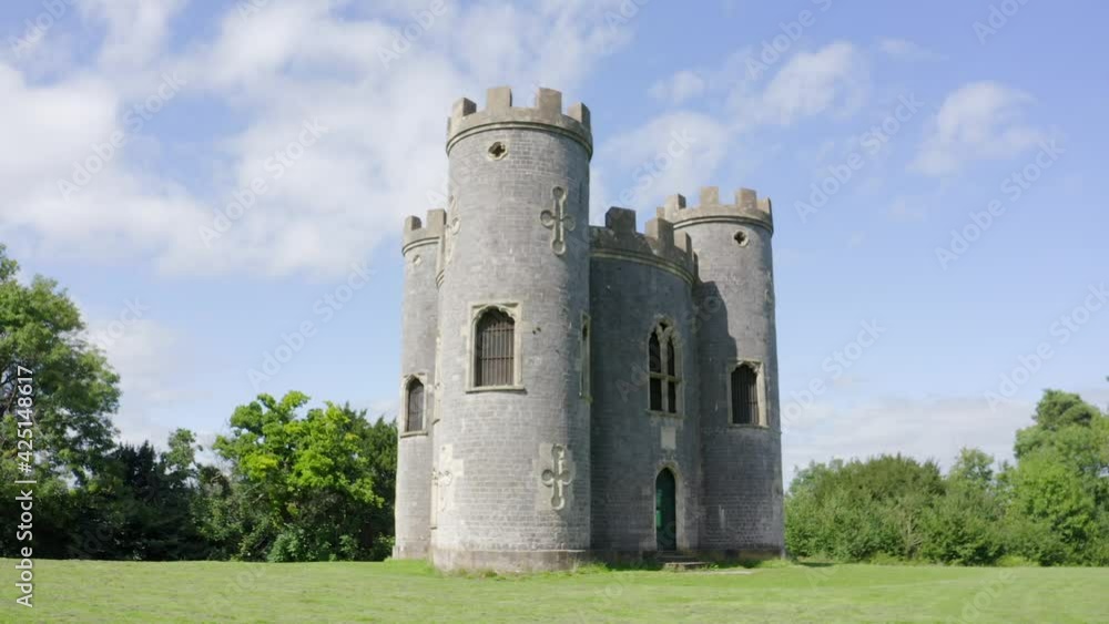 Low aerial around 18th century gothic British folly castle with three turrets on a sunny day with trees in the background. High quality 4k footageLow aerial around 18th century gothic British folly Low aerial around 18th century gothic British folly castle with three turrets on a sunny day with trees in the background. High quality 4k footageLow aerial around 18th century gothic British folly