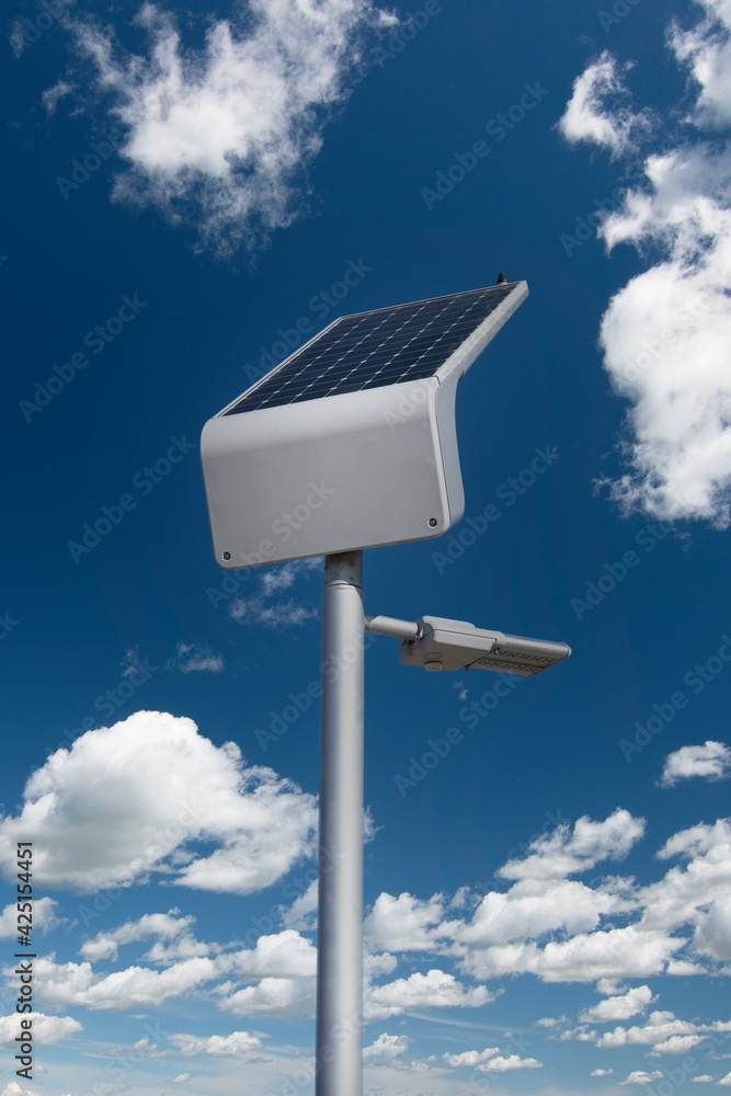 A solar powered street light on a lamp post recharging in the sun on a cloudy summer day.