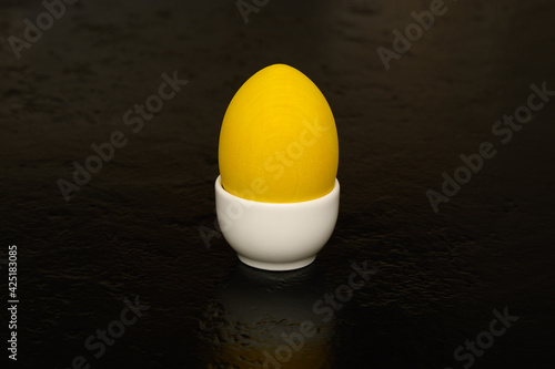 Yellow wooden egg in a white porcelain egg holder on a black background
