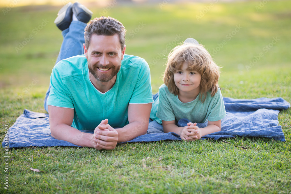 Father and son laying on grass in park. People having fun outdoors. Concept of happy vacation and friendly family. Father and son laying on grass in park. People having fun outdoors. Concept of happy vacation and friendly family.