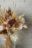 Beautiful dried flower bouquet in glass vase near white brick wall