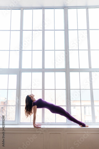 A beautiful dark-haired girl in a sports purple jumpsuit performs yoga asanas. Healthy lifestyle, sports. © Ольга Апанасенко