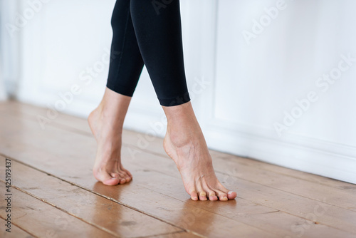a photo of feet on cusps  in black leggings on a wooden floor against a white wall. Yoga therapy. Exercise for the legs.