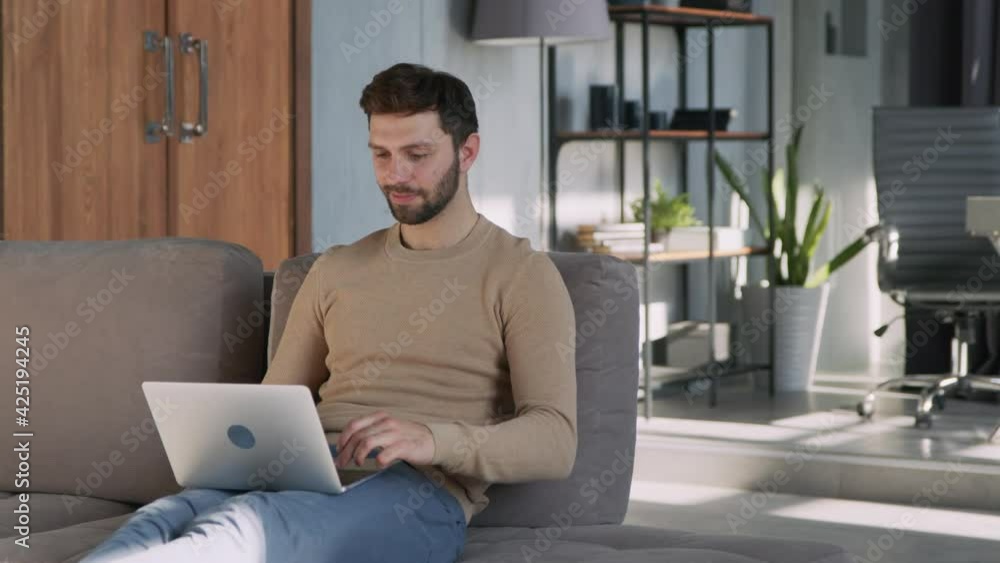 Smiling man typing freelancer with laptop on couch at home. Smiling man typing freelancer with laptop on couch at home.