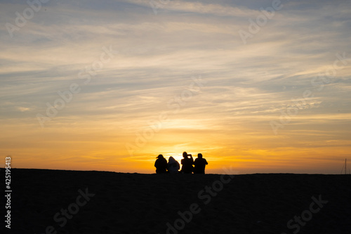 Silhouette of four people sitting at the beach watching the sunset. © Martin