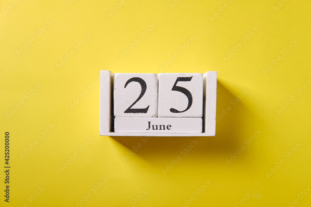 Wooden calendar on yellow background, top view, date 25 June Wooden calendar on yellow background, top view, date 25 June