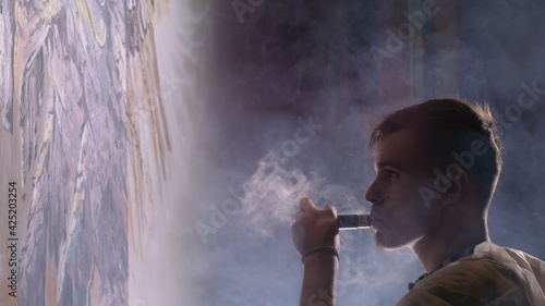 Artist designer draws an eagle on the wall. Craftsman decorator paints a picture with acrylic oil color. Vaper smokes vape. Dark magic cinematic look. photo