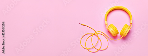 Yellow headphones on pink banner. Minimal Music concept, flat lay, copy space