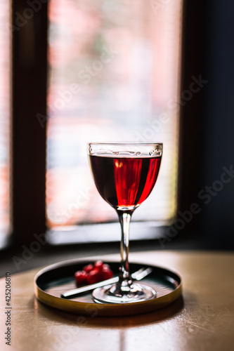 A red alcoholic cocktail in a nick and nora glass served on a tray with cranberry garnish, shot with back light. A lifestyle vertical photo with shallow depth of field.