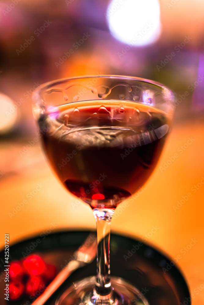 A red alcoholic cocktail in a nick and nora glass served on a tray with cranberry garnish. A lifestyle photo with shallow depth of field.