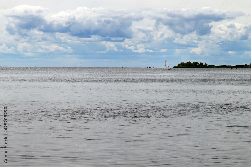 The gray cold sea under the cloudy sky. A small sail of a yacht can be seen in the distance. The gray cold sea under the cloudy sky. A small sail of a yacht can be seen in the distance.